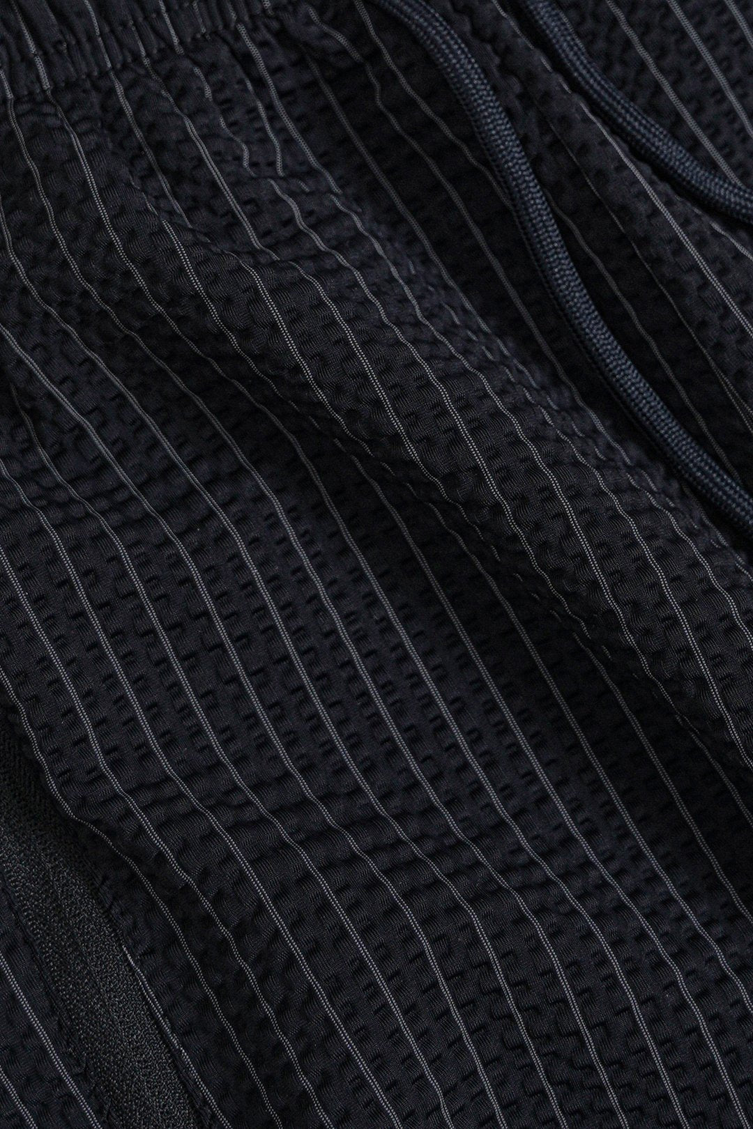 Close-up of dark charcoal gray textured fabric with thin vertical pinstripes and a matching drawstring.