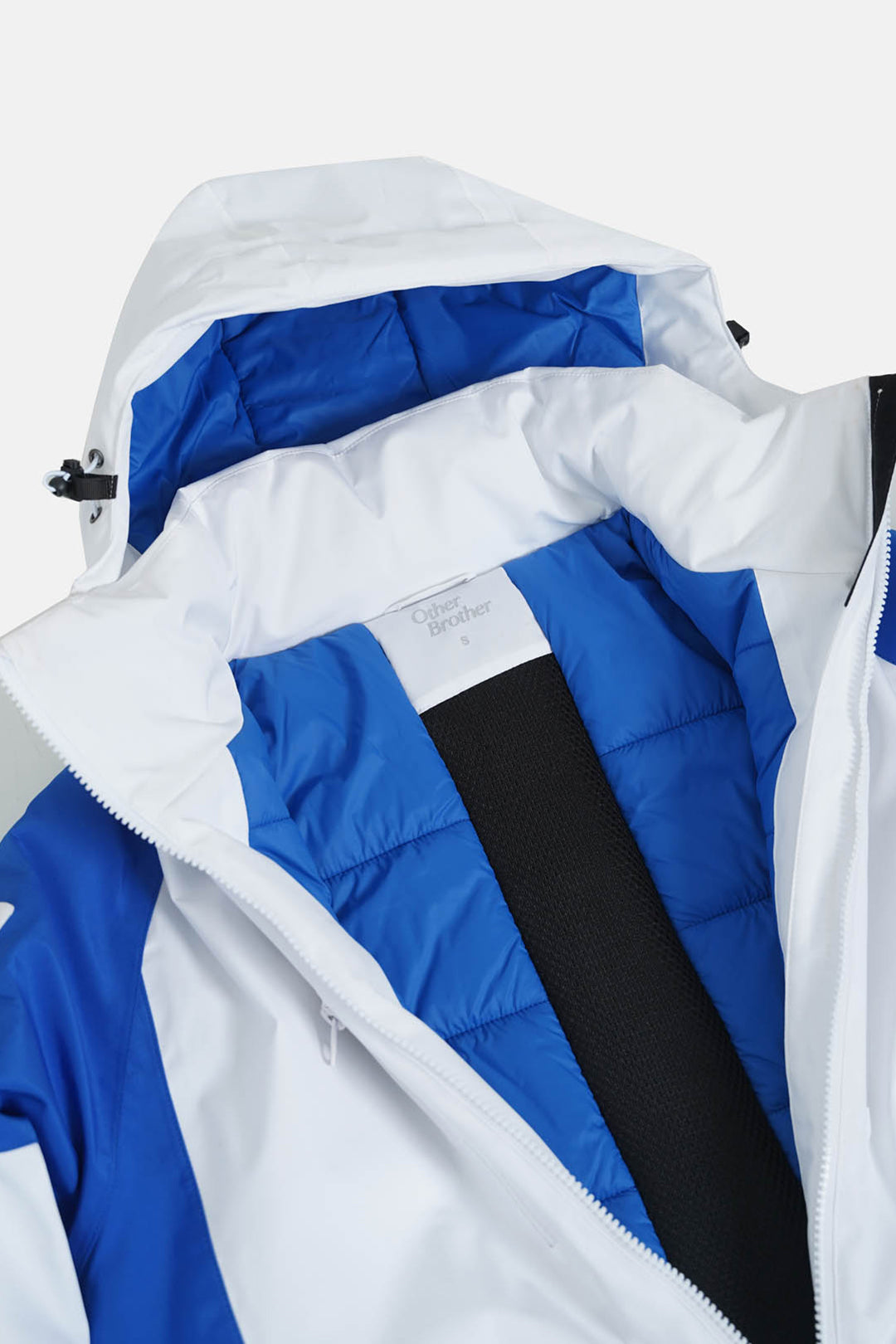 Image of Close-up of a hooded puffer jacket with a white and royal blue color-blocked design, featuring a black inner lining and a white neck label.