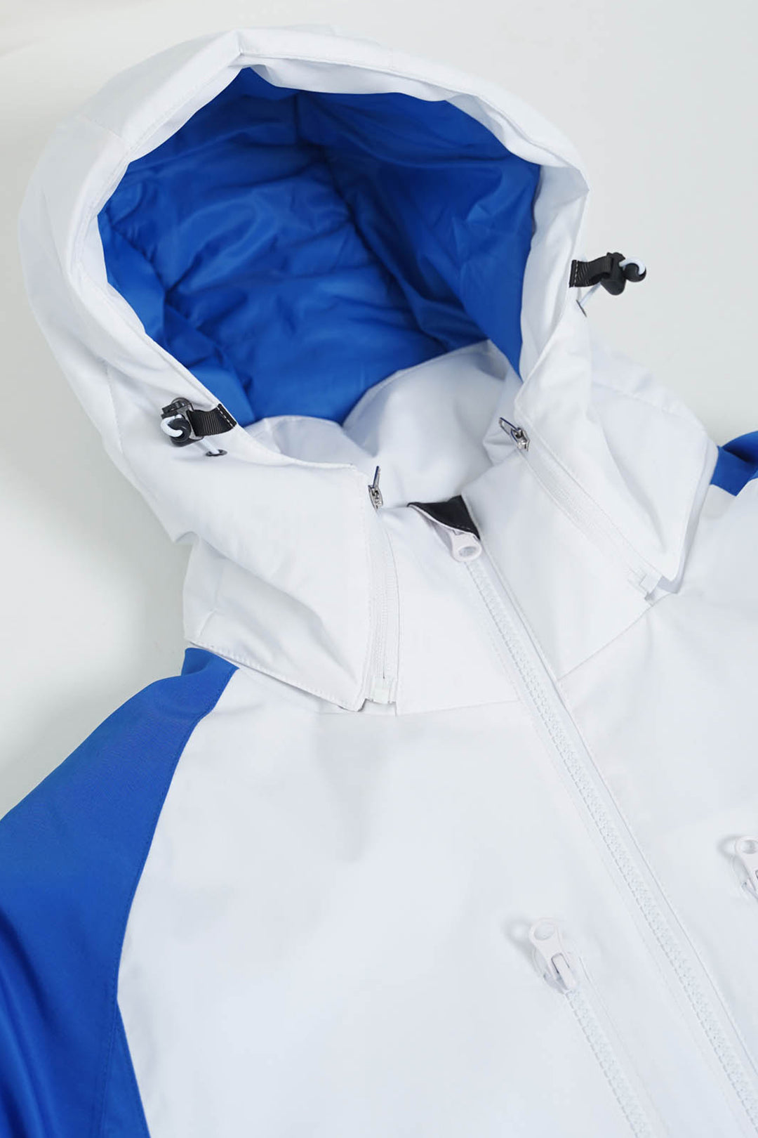 A close-up of a white and royal blue hooded jacket, showing the white outer shell, front zipper, and bright blue inner hood lining.