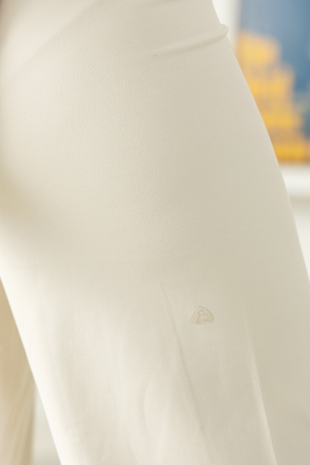 Image of A close-up of a light cream or off-white fabric surface with a small tonal embroidered logo near the lower center.