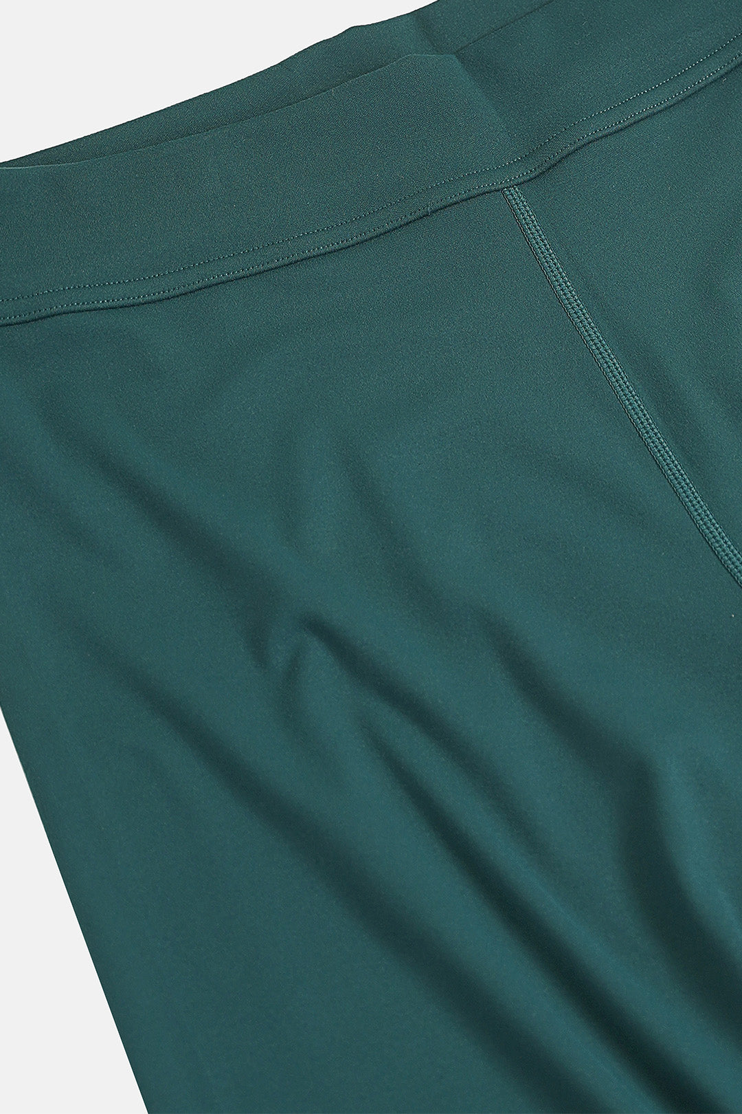 Image of Close-up of dark teal green athletic leggings showing the waistband seam and fabric texture.