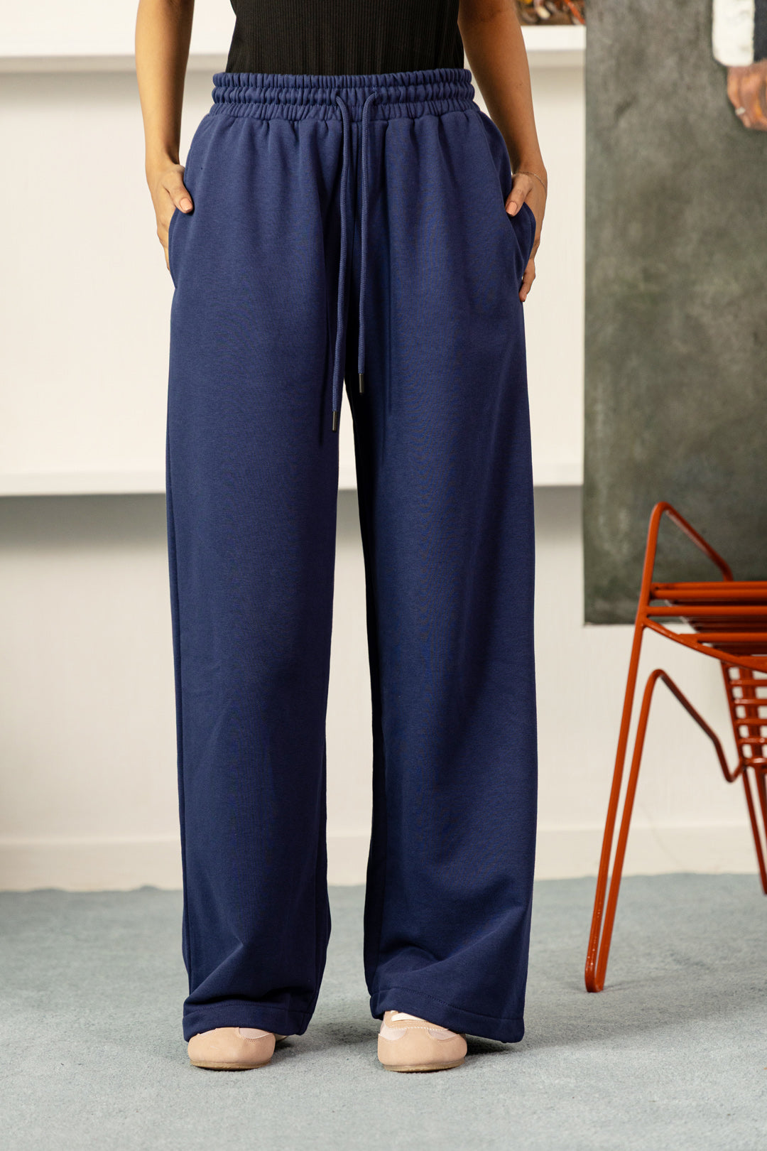 A person wearing navy blue wide-leg sweatpants with an elastic drawstring waist and side pockets, standing indoors on a gray floor.