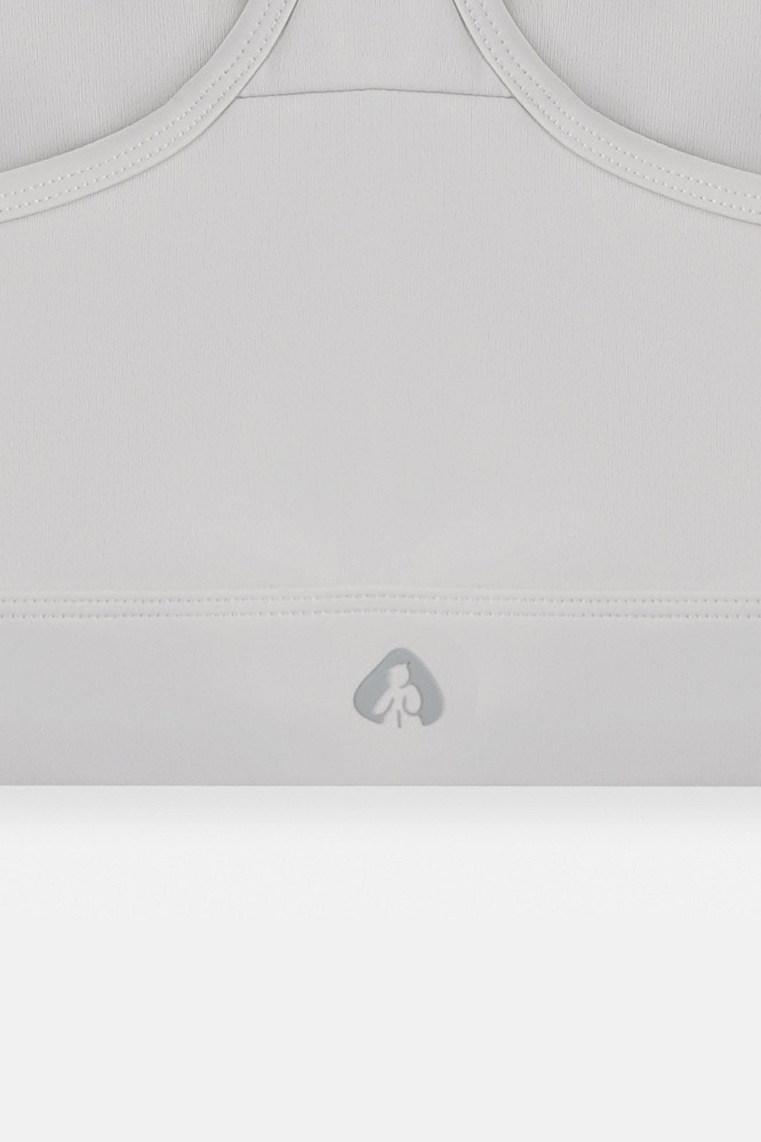 Close-up of a light gray sports bra or athletic top showing the underband with a small gray logo and ribbed neckline.
