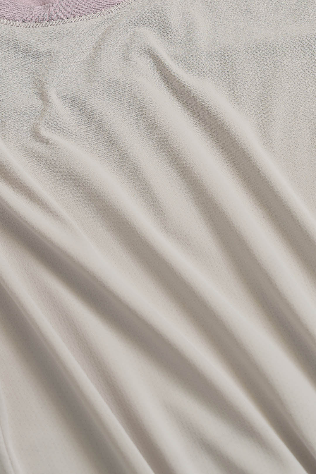 Image of A close-up of a light cream or off-white fabric with soft folds and a small sliver of pale pink visible at the top edge.