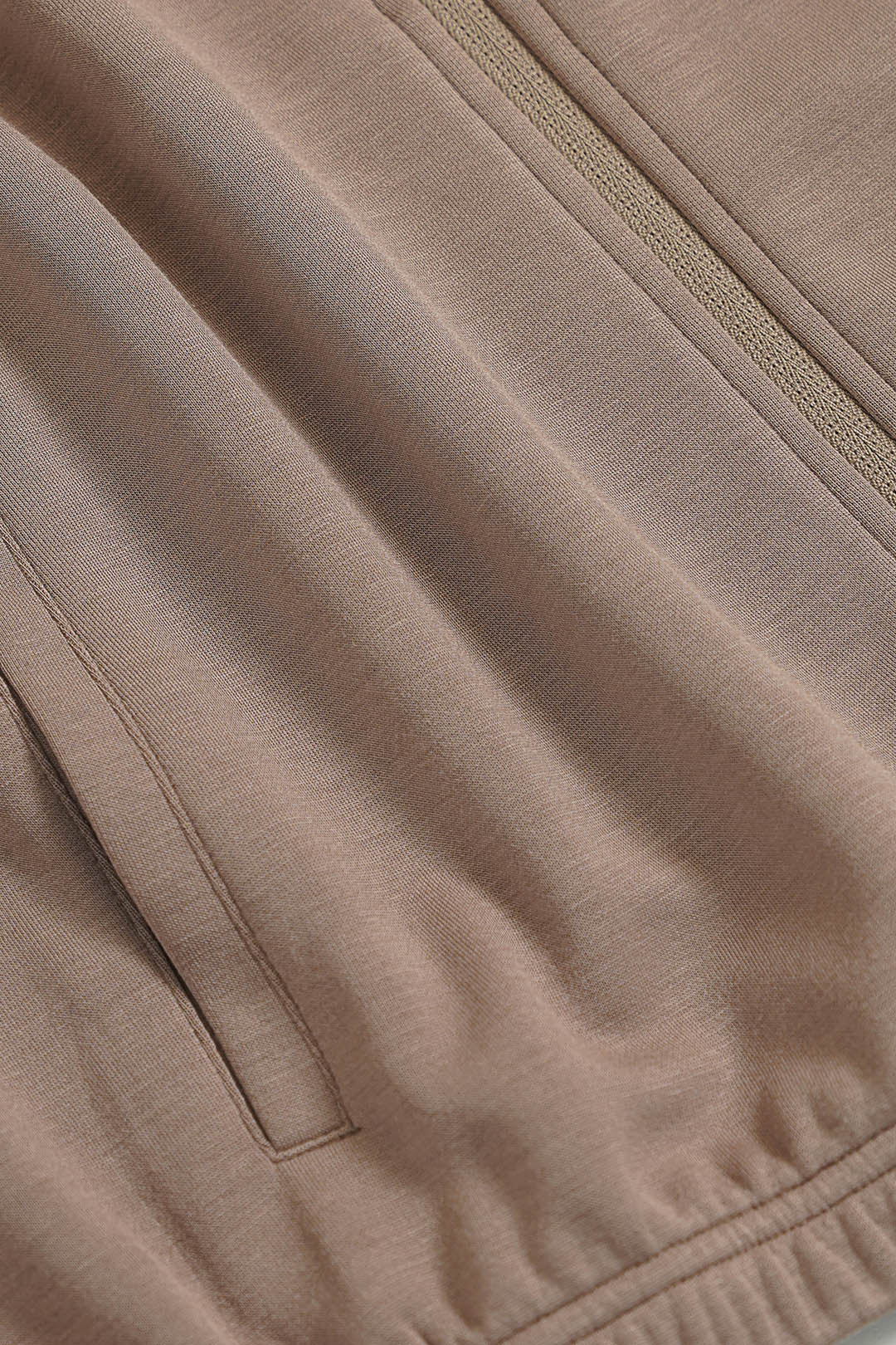 Image of Close-up of a taupe-beige knit fabric with a zippered pocket and matching zipper detail.