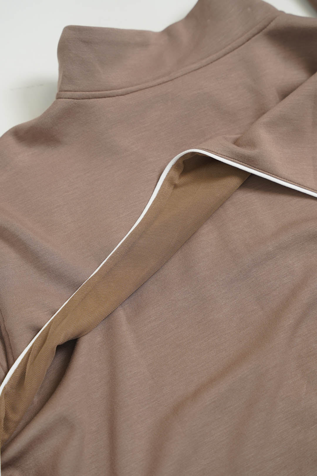 Close-up of a taupe brown knit garment with a high mock neck and a contrasting white piping trim along the collar.