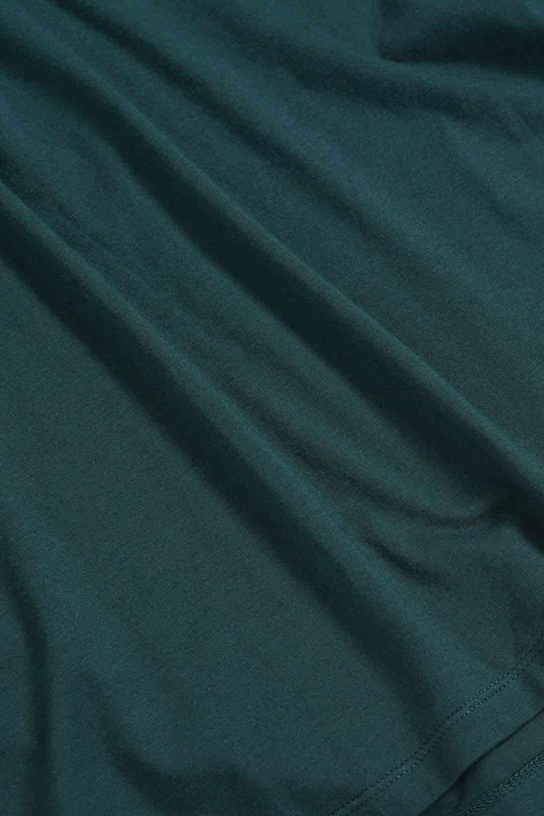 Image of A close-up of dark  green fabric with soft folds and a visible hem.