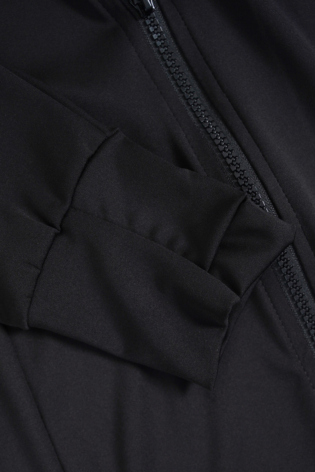 Close-up detail of a black softshell jacket showing a zippered pocket and a black zipper.