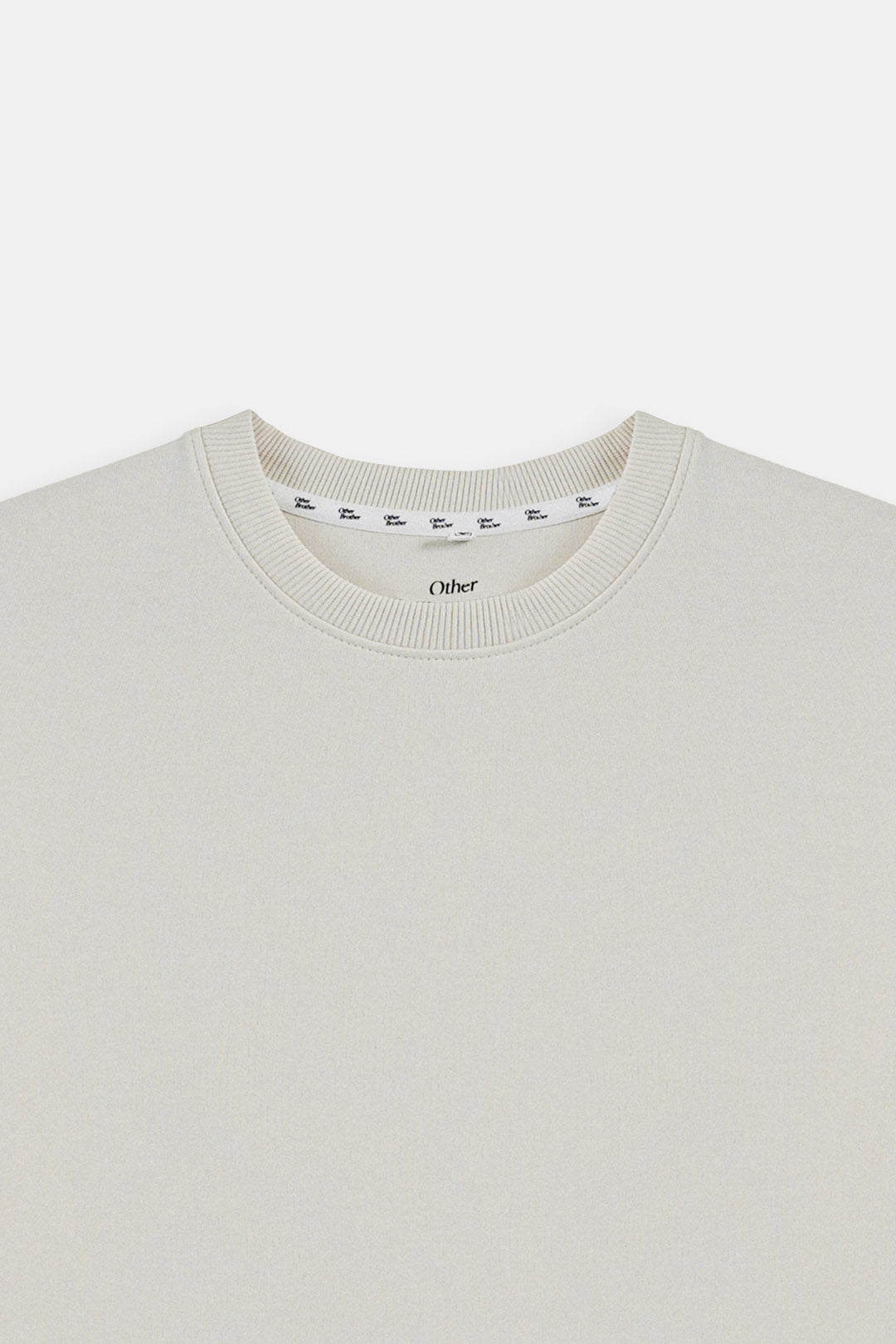 Close-up of a crewneck sweater in a light cream or off-white color, showing the ribbed collar and a visible inner neck label with the brand name 'Older'.