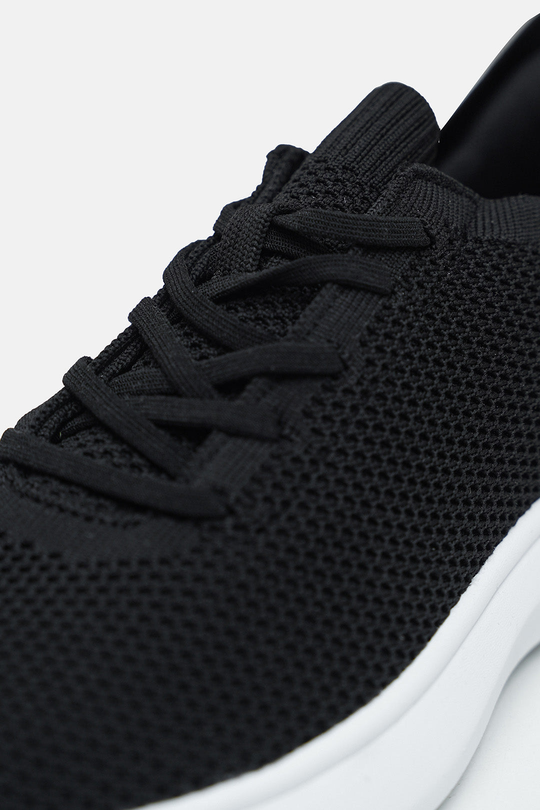 Image of Close-up of a black knit sneaker with black laces and a white sole, shown against a light gray background.